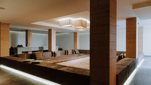 A modern living room with a large sectional sofa, wooden beams, and a long wooden bench. - Hubers Boutiquehotel (Mayrhofen)