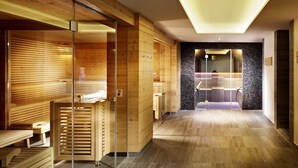 A modern spa with wooden paneling, glass doors, and a central seating area. - Hubers Boutiquehotel (Mayrhofen)