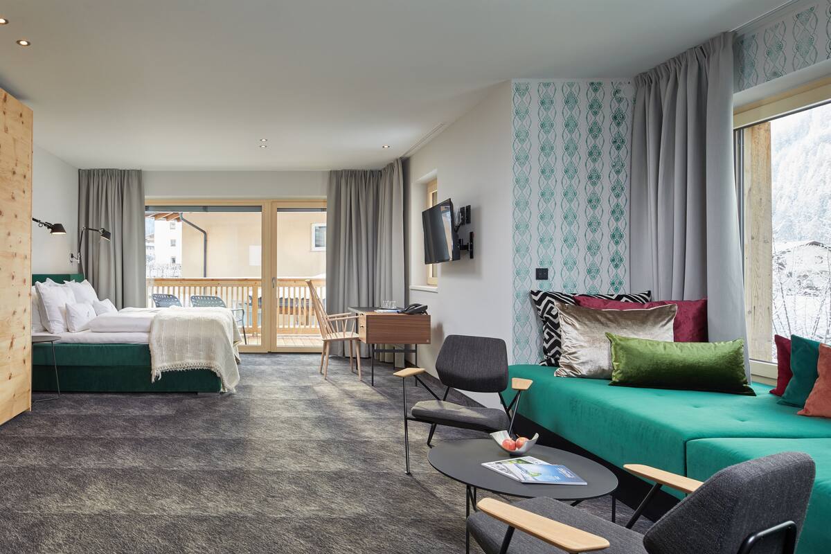 Una habitación de hotel con una cama, un sofá verde, un escritorio, una silla y un televisor.
