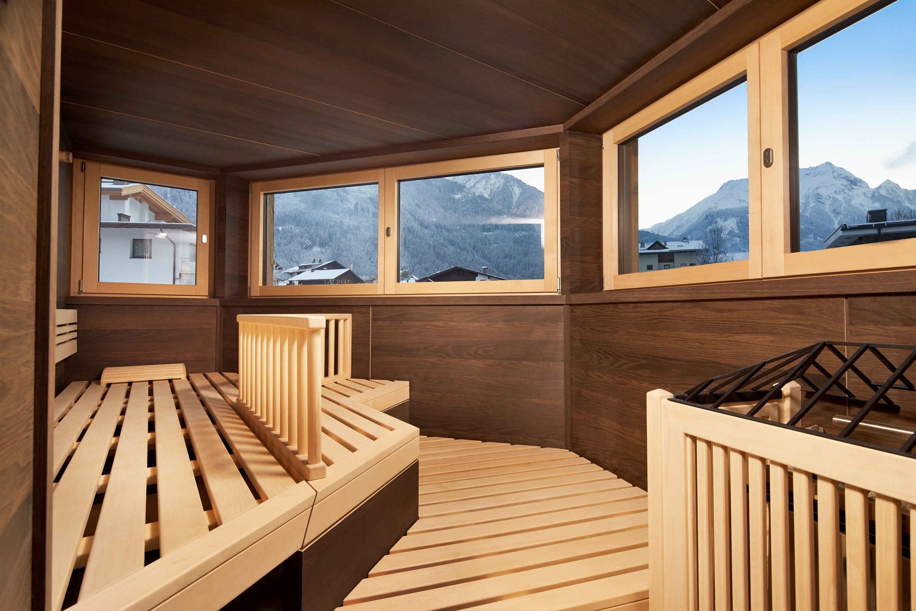 A wooden spa room with a wooden bench and a view of mountains through large windows.