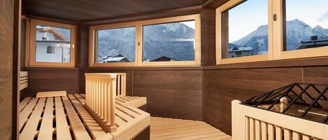 A wooden spa room with a wooden bench and a view of mountains through large windows.