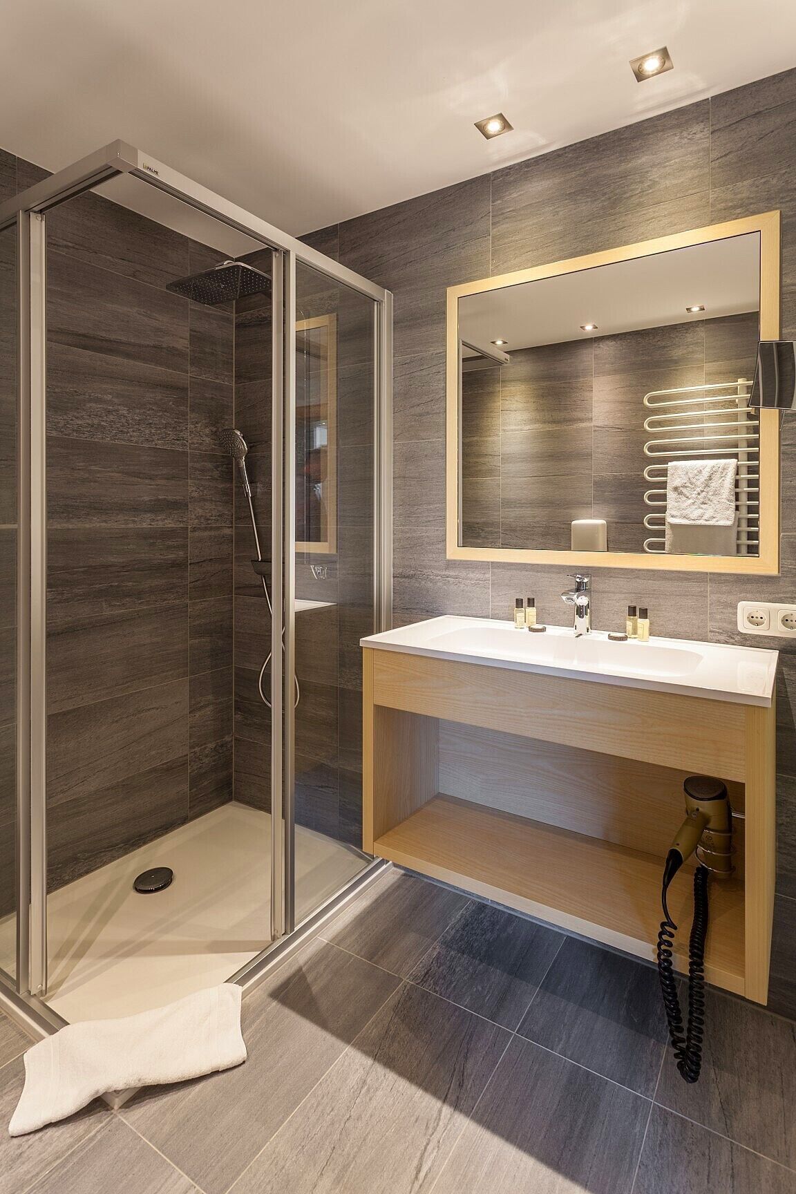 Un baño moderno con ducha envuelta en vidrio, tocador de madera y un espejo grande.