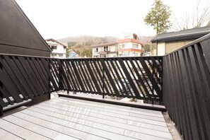 A wooden balcony with a view of residential buildings and hills in the background. - Tanuki Nozawa (Nozawaonsen)