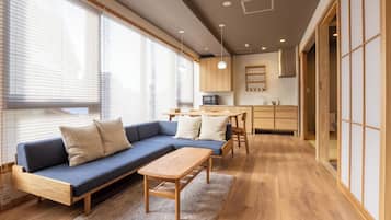 Una sala de estar moderna con un sofá azul, una mesa de centro de madera y una cocina al fondo.