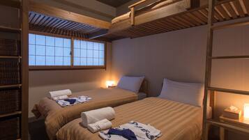 A room with two beds, wooden bunk beds above, a window with a view, and a shelf with baskets.