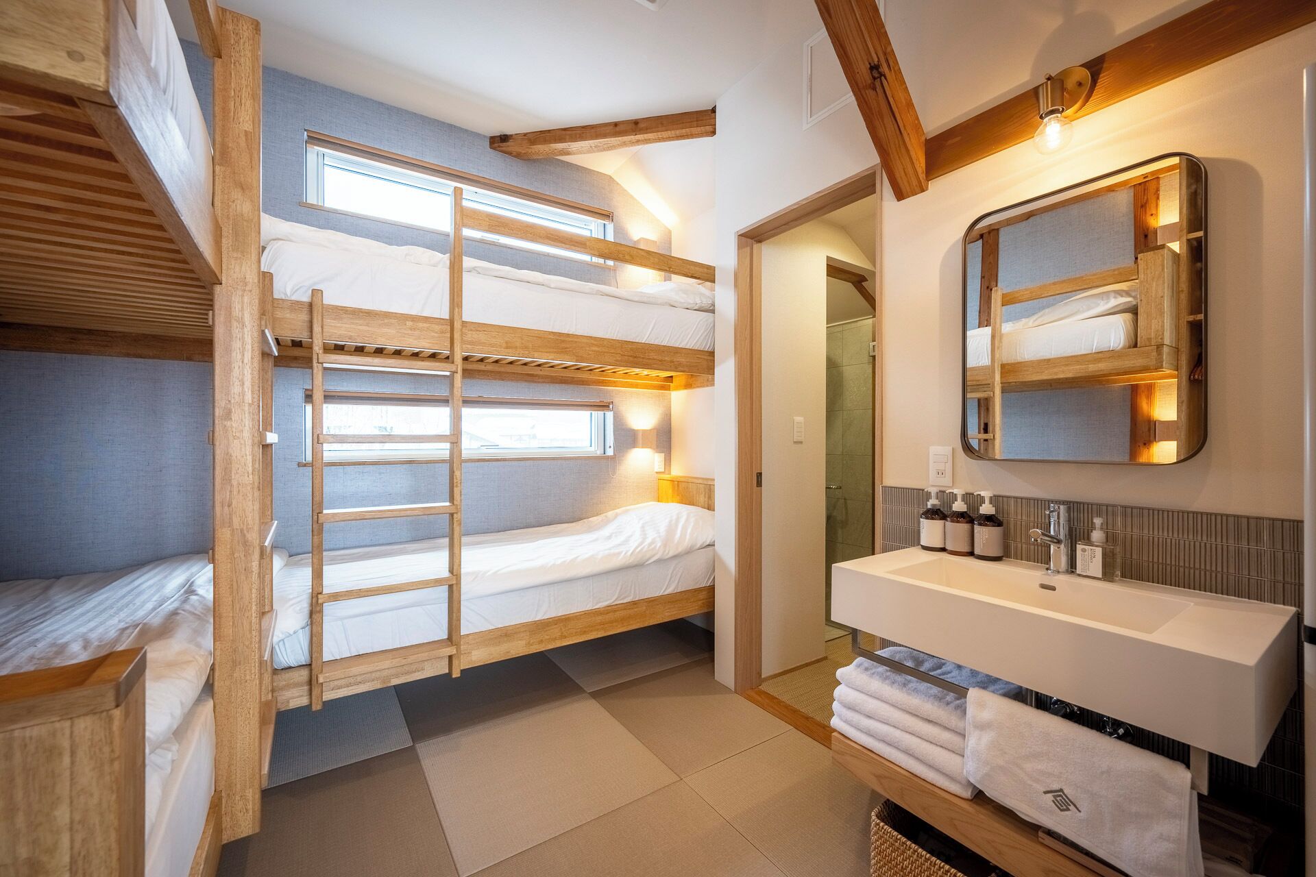 A compact, well-lit room with bunk beds, a bathroom with a sink and mirror, and a visible shower area.