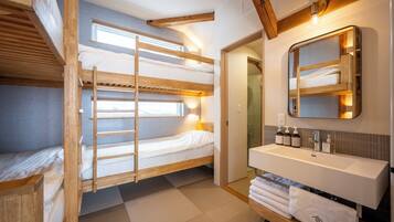 A compact, well-lit room with bunk beds, a bathroom with a sink and mirror, and a visible shower area.