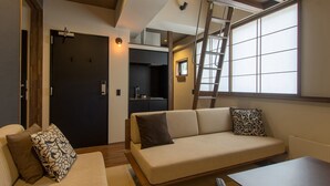 A modern living room with a sofa, a coffee table, and a kitchen area in the background. - Tanuki Nozawa (Nozawaonsen)