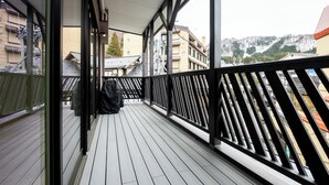 A wooden deck with a black railing, overlooking a snowy mountain and buildings. - Tanuki Nozawa (Nozawaonsen)