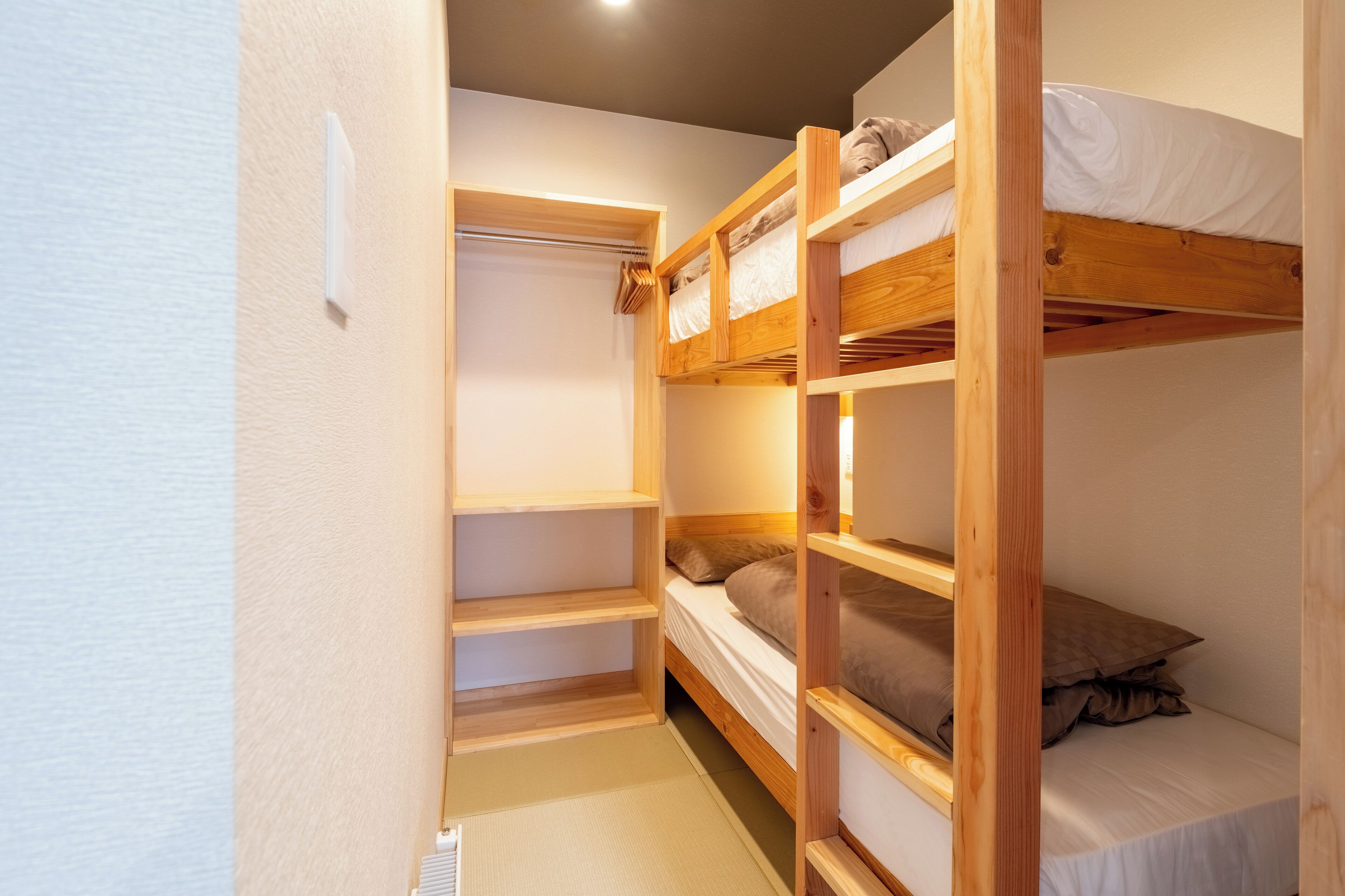 A bunk bed room with a wooden ladder, a small closet, and a single bed with a pillow.