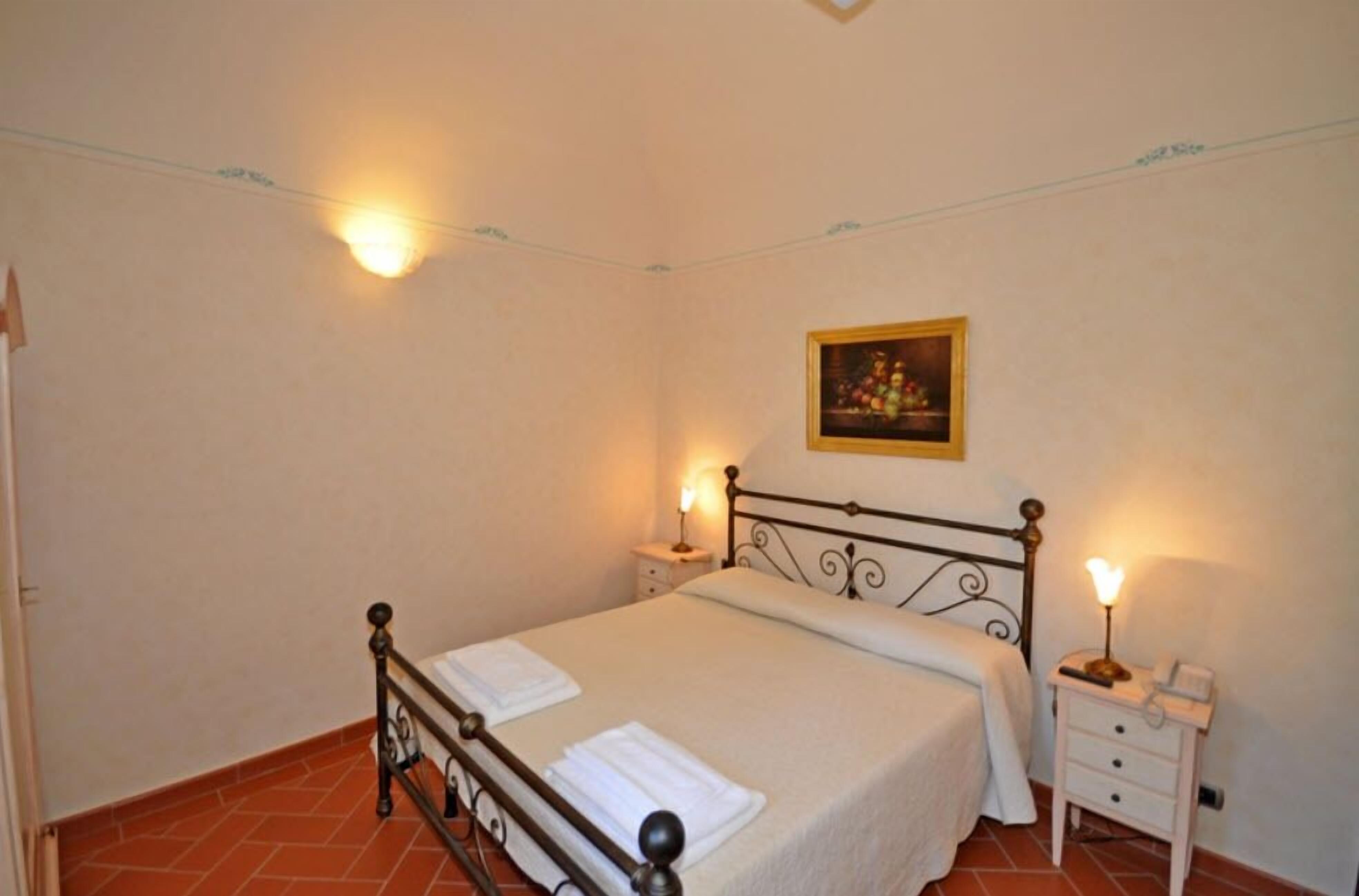 A bedroom with a bed, bedside tables, and wall-mounted lights.