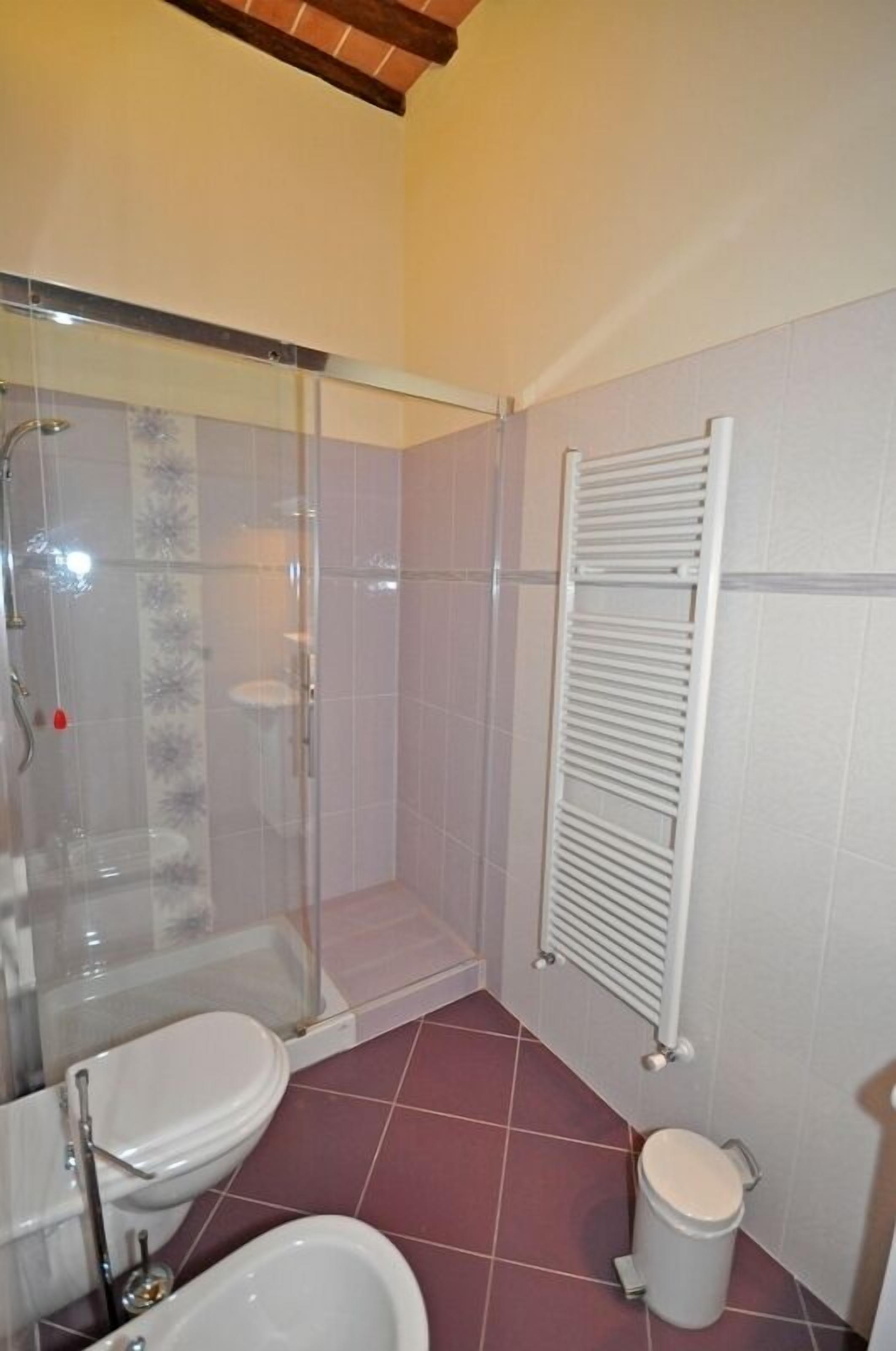 A bathroom with a glass-enclosed shower, a toilet, a bidet, and a white radiator.