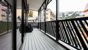 Eine Holzterrasse mit schwarzer Reling, mit Blick auf einen verschneiten Berg und Gebäude.