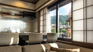 Eine moderne Küche mit Blick auf einen Berg und Gebäude, eine Sitzecke mit Sofa und Sesseln sowie ein großes Fenster mit Aussicht.