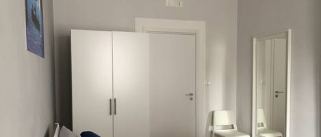 A hotel room with a bed, a wardrobe, a chair, a mirror, and a small table with a towel.