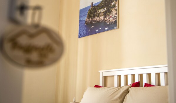 A bedroom with a bed, a wall-mounted picture of a coastal scene, and a circular object on the wall. - B & B Raffaello (Terzigno)