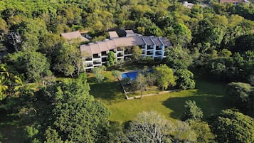 A multi-story building surrounded by lush greenery, with a swimming pool and a well-maintained lawn.