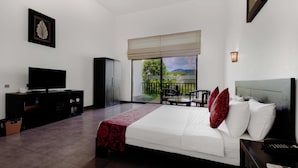 Une chambre à coucher comprenant un lit, une télévision, une armoire, un coin repas avec des chaises et une vue sur l’extérieur.