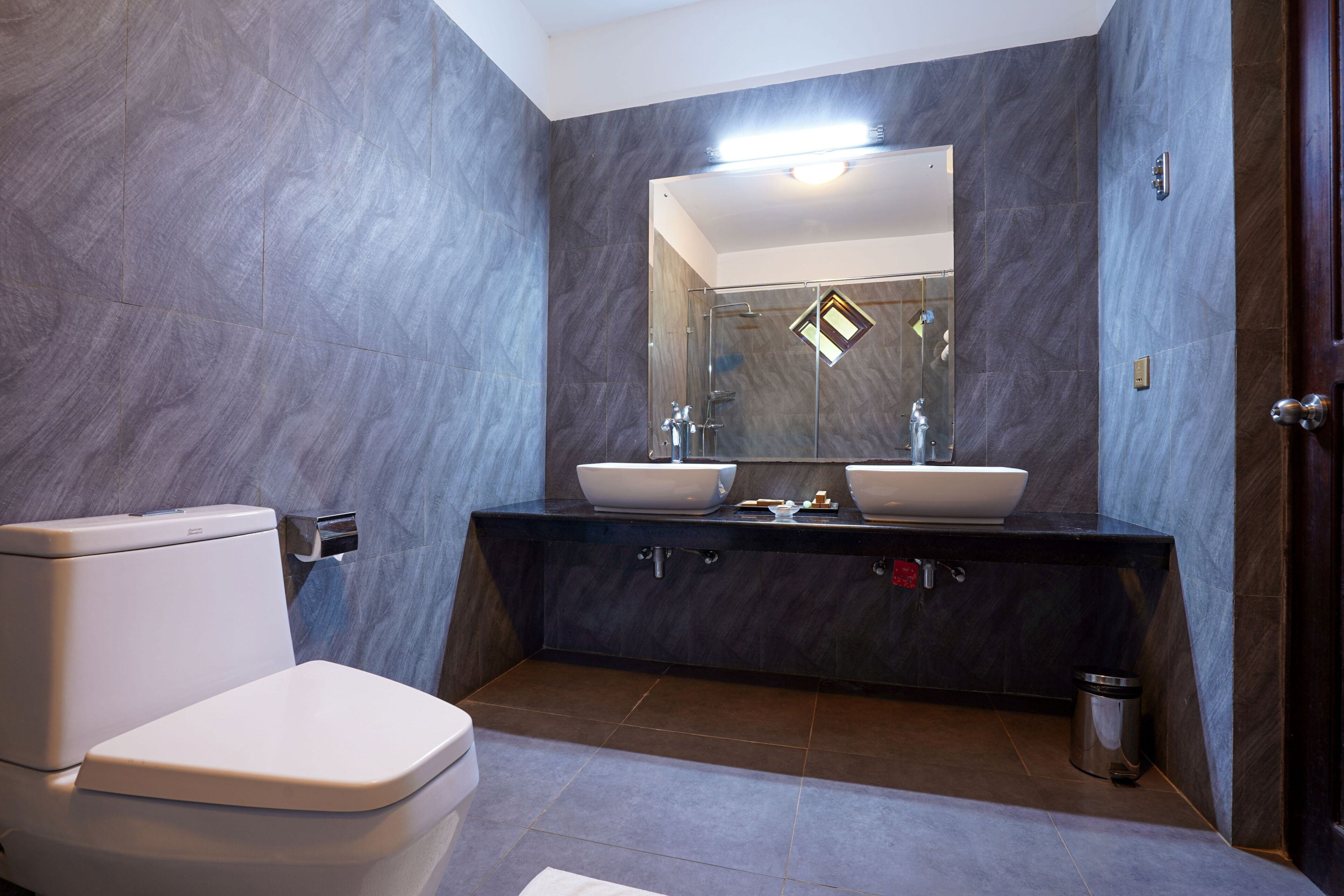Une salle de bain moderne avec des toilettes, deux lavabos et un miroir.