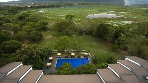 Zona de piscina con vistas a montañas, rodeada de vegetación exuberante y algunos edificios a lo lejos.