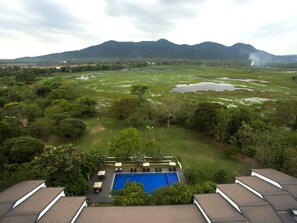 Ein Poolbereich mit Bergblick, umgeben von üppiger Vegetation und einigen Gebäuden in der Ferne.