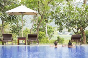 Ein Poolbereich mit einer Person, die im Wasser entspannt, umgeben von Bäumen und Gartenmöbeln.