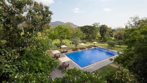 Una piscina rectangular rodeada de sillas de descanso y sombrillas, con vistas a un paisaje montañoso.