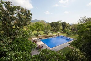Ein rechteckiger Swimmingpool, umgeben von Liegestühlen und Sonnenschirmen, mit Blick auf eine gebirgige Landschaft.