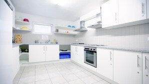 A modern kitchen with white cabinets, a stove, oven, and a blue storage bin. - Hotel Victoria (Weil am Rhein)