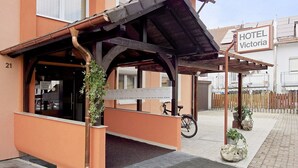 A hotel entrance with a covered waiting area, a sign reading "HOTEL Victoria," and a bicycle parked outside. - Hotel Victoria (Weil am Rhein)