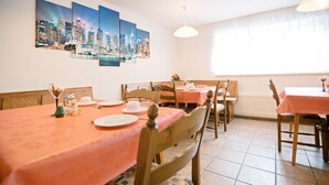 A dining area with tables set for four, wooden chairs, and a cityscape mural on the wall. - Hotel Victoria (Weil am Rhein)