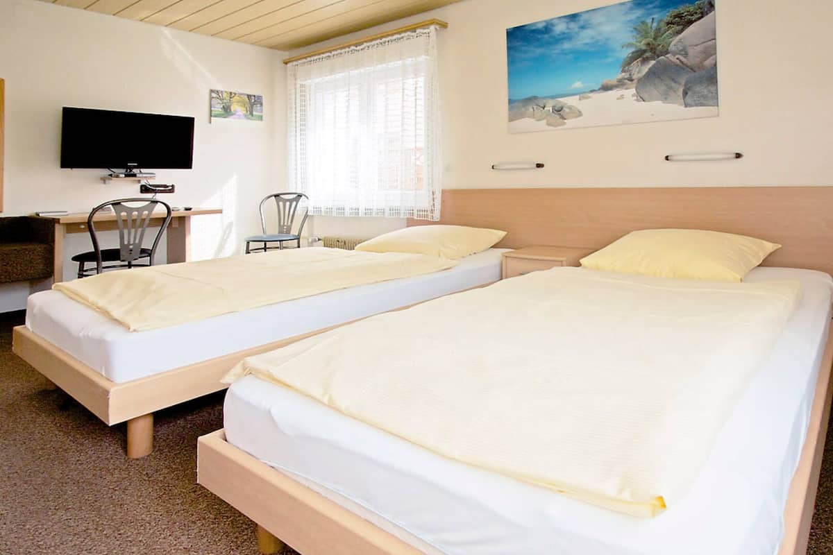 Une chambre d’hôtel avec deux lits simples, un bureau avec une chaise, une télévision et une fenêtre avec des rideaux.