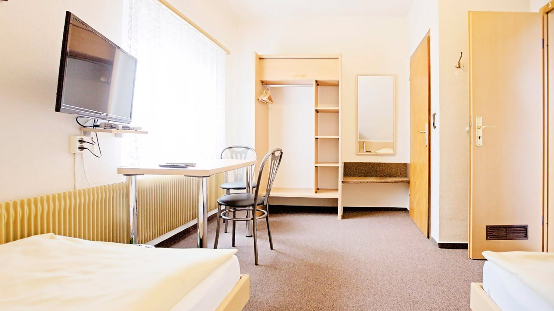A hotel room with a bed, a desk, a chair, a television, a wardrobe, and a bathroom mirror.