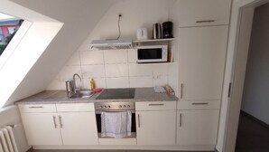 A compact kitchen with a gas stove, microwave, and a small oven. There is a window providing natural light, and the kitchen has white cabinets and a tiled backsplash. - Hotel Victoria (Weil am Rhein)