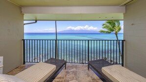 Un balcon avec deux lits, une vue sur l’océan et un palmier.