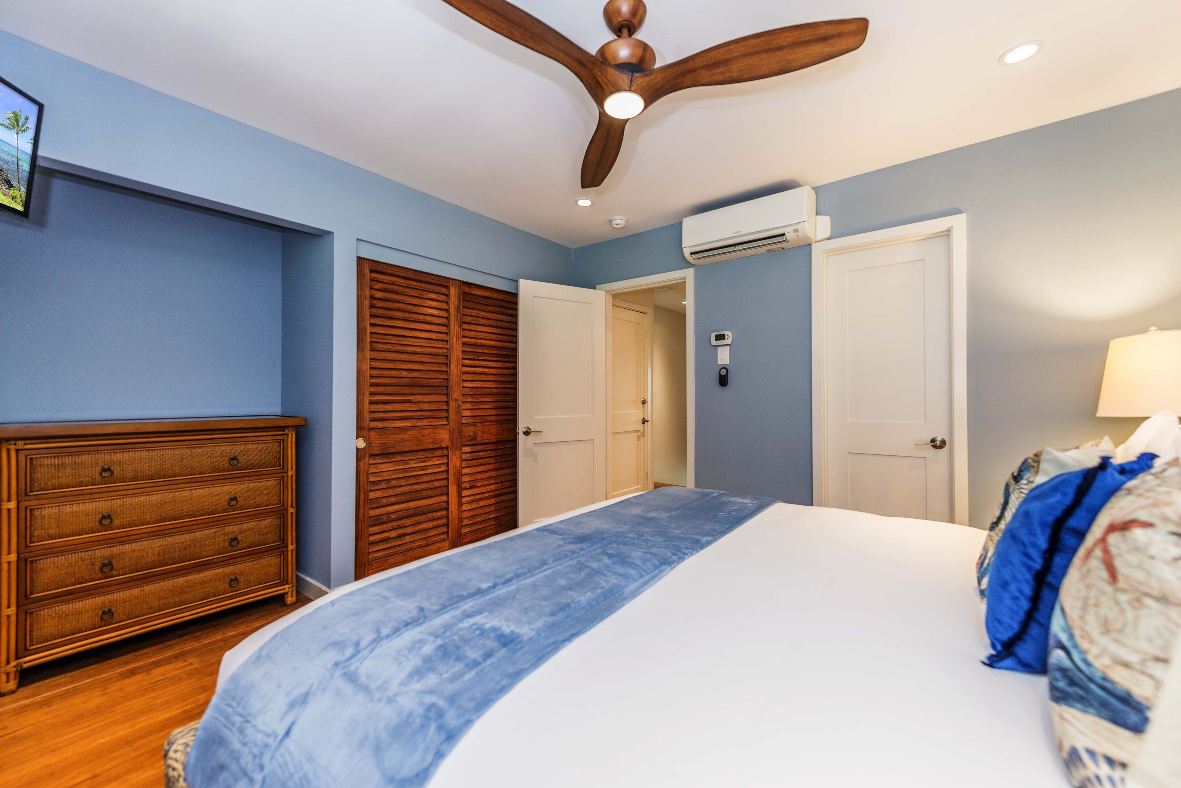 A bedroom with a bed, wooden dresser, and a ceiling fan.
