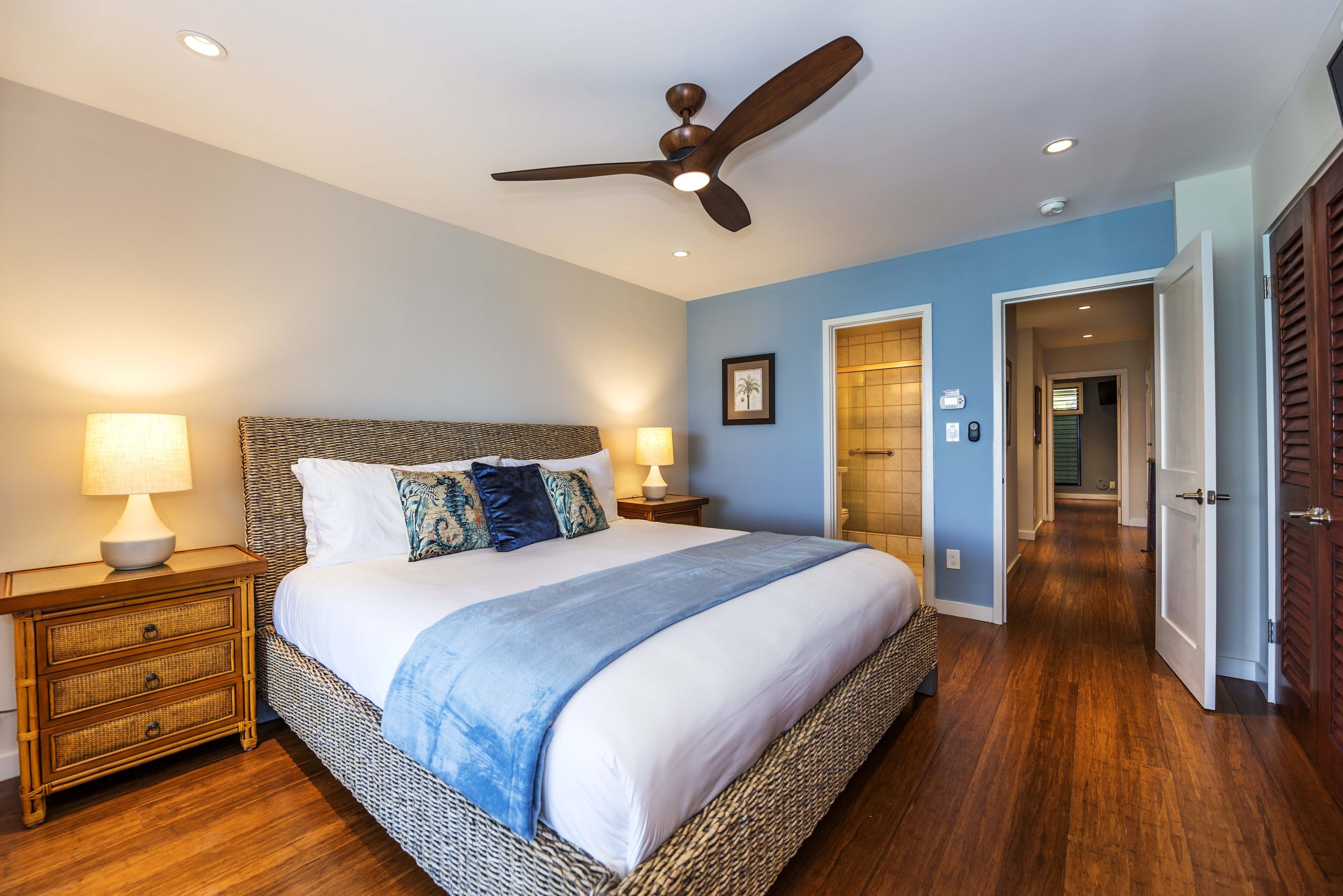 A bedroom with a large bed, two bedside tables with lamps, a ceiling fan, and a wooden floor.