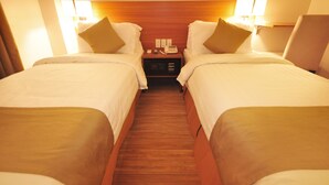 A hotel room with two single beds, a wooden headboard, bedside lamps, a nightstand with a phone and a lamp, and a wooden floor. - Baypark Inn (Calbayog)