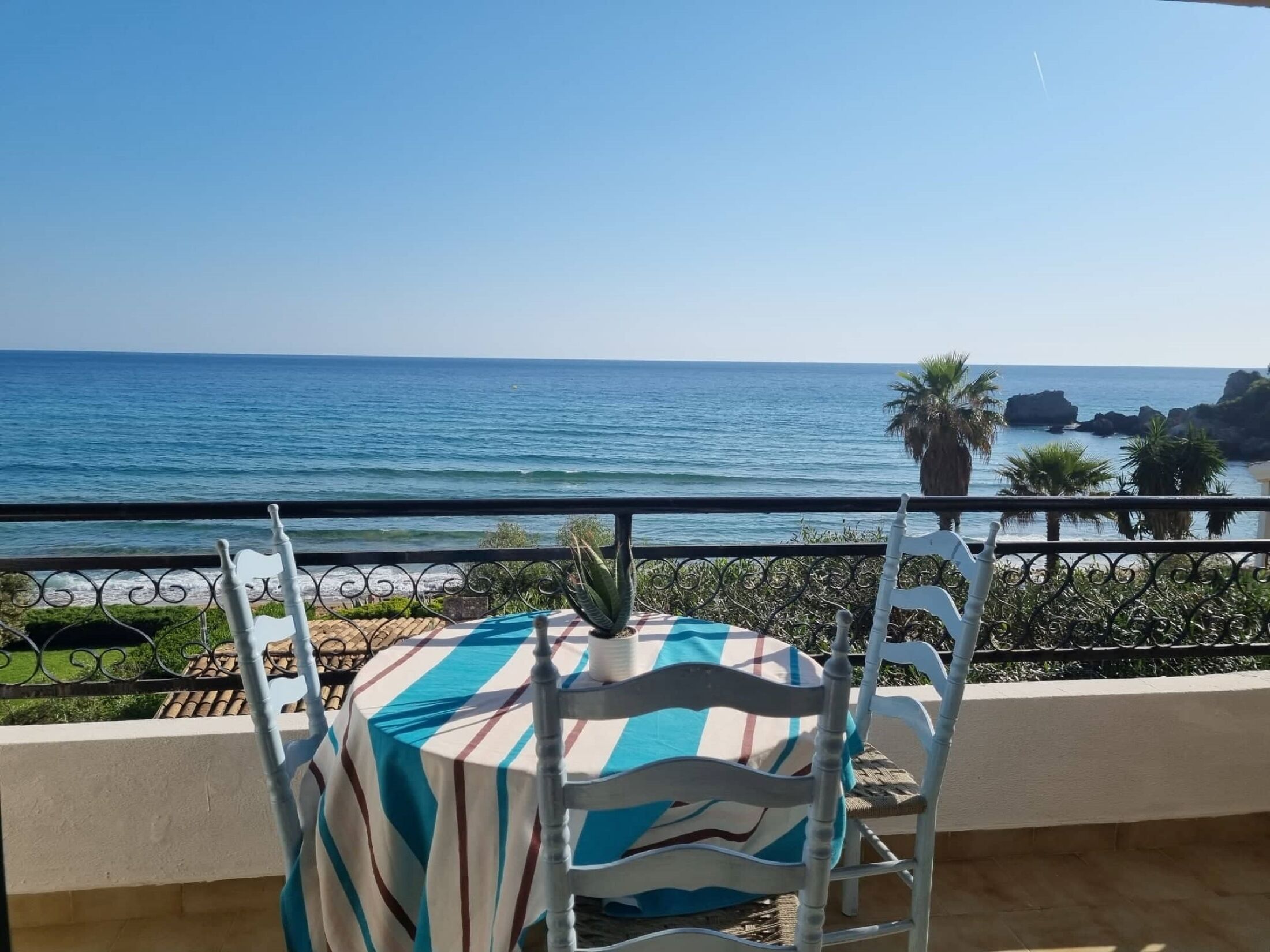 Un balcon avec une table et des chaises, offrant une vue sur la côte, la mer et les formations rocheuses.
