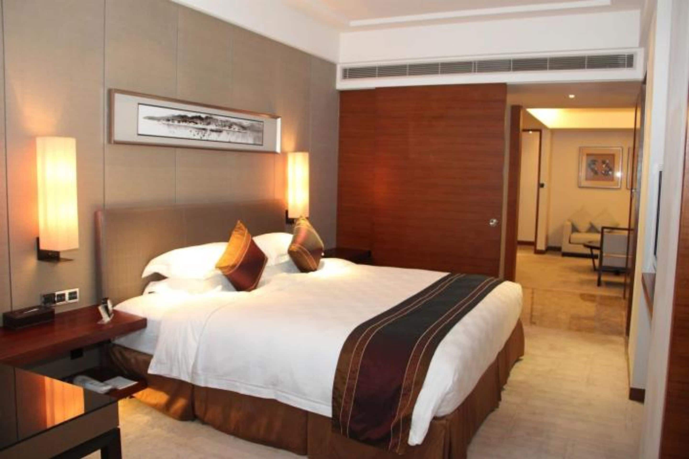Habitación de hotel con una cama grande, dos mesitas de noche, cabecera y un cuadro en la pared.