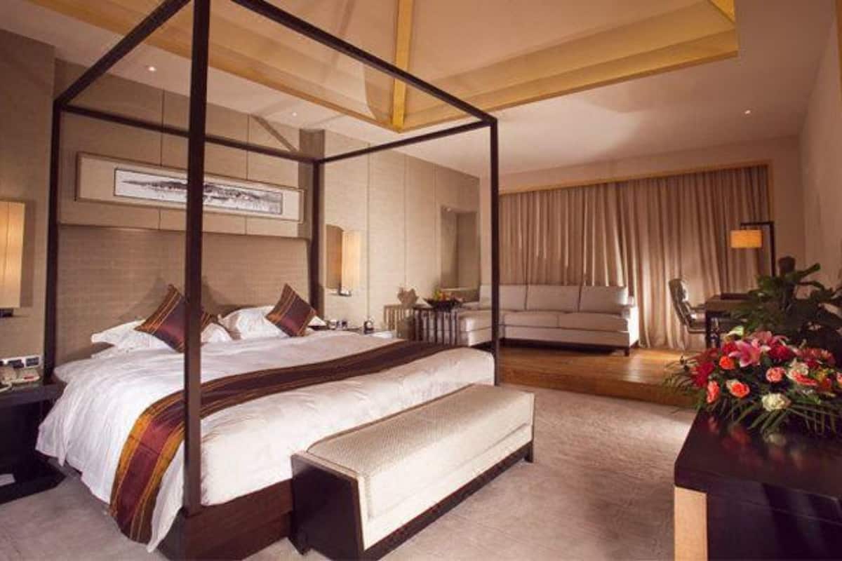 Moderni hotellihuone, jossa on nelipylväinen sänky, sohva, työpöytä ja suuri ikkuna, jossa on verhot.