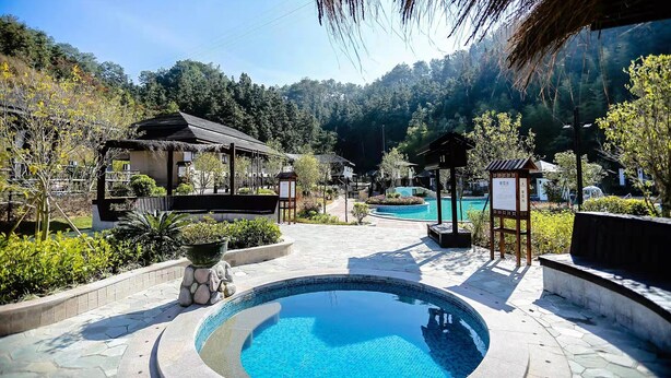 A pool area with a stone border, a thatched-roof structure, and a signboard. - Heyuan Mels Welton Evergreen Lake Hotel (Heyuan)
