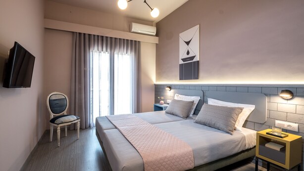 Una habitación de hotel moderna con una cama grande, una mesita de noche, una silla, un televisor y un ventanal con cortinas.
