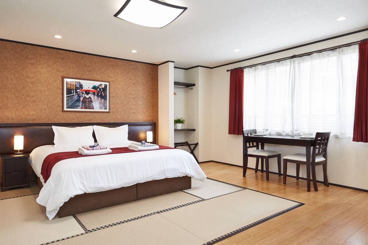 A hotel room with a large bed, a desk with chairs, and a window with curtains.