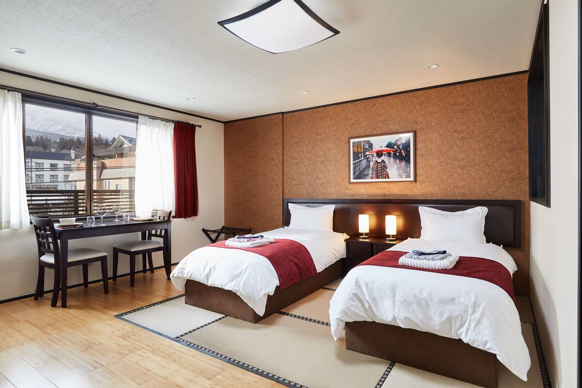 A hotel room with two beds, a dining table, and a view of the city.