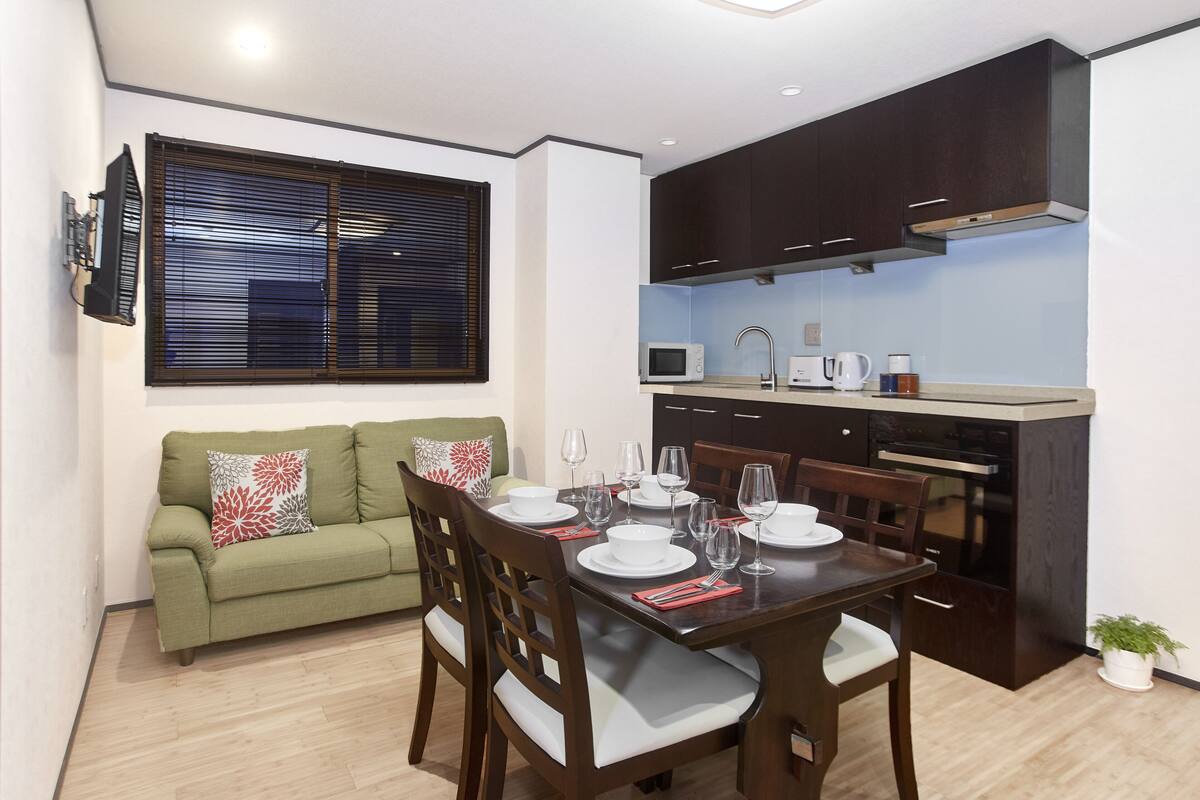 A compact living space with a dining area, kitchenette, and a green sofa with patterned cushions.