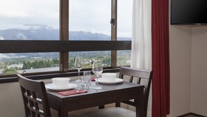 Une table à manger avec de l’assiette blanche, des verres et une serviette rouge, le tout placé devant une fenêtre offrant une vue sur les montagnes.