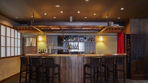 Un espace bar doté d’un comptoir en bois, de quatre tabourets et d’une variété de bouteilles et de verres.