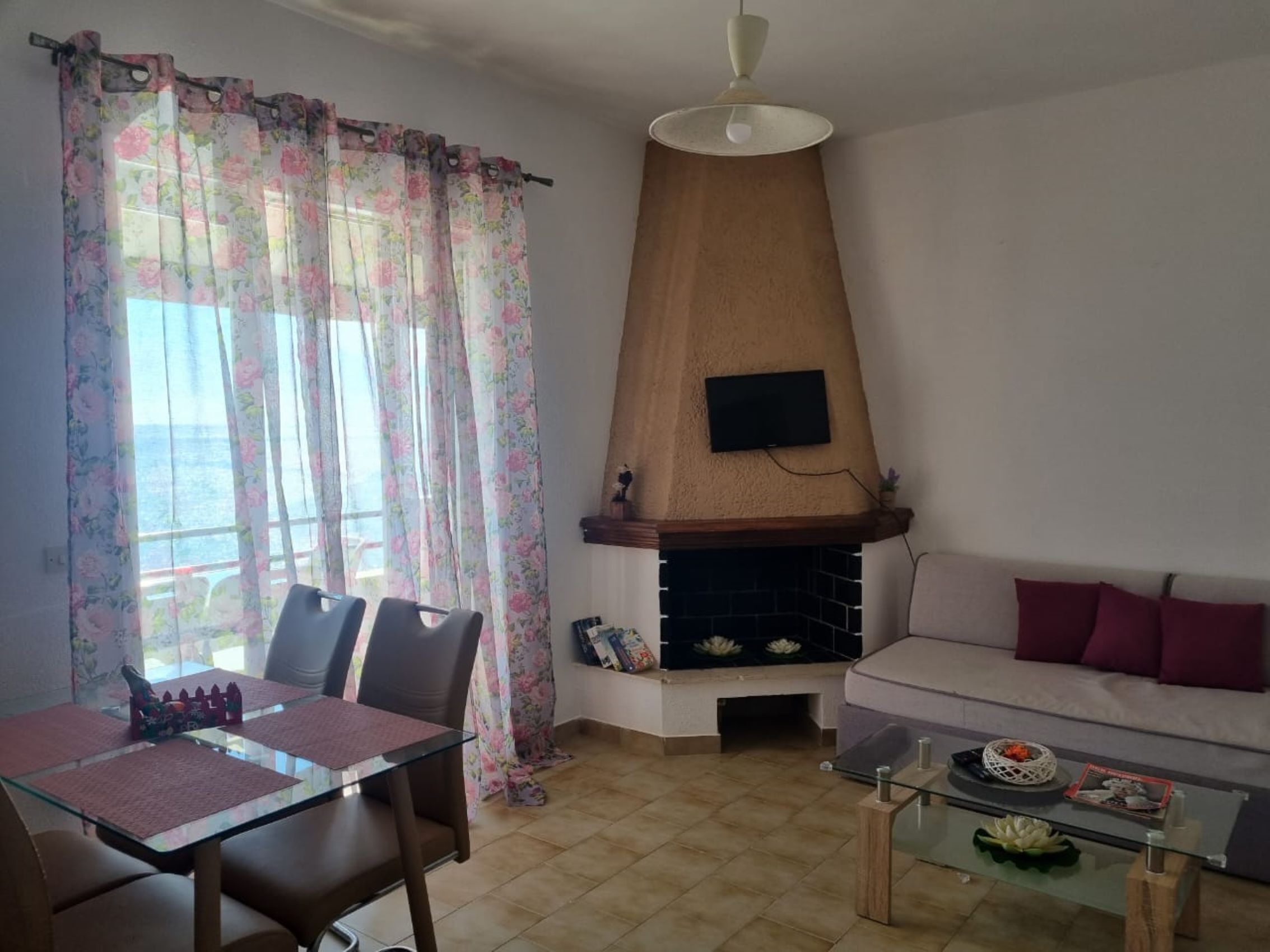 A living room with a sofa, a fireplace, a dining table with chairs, and a TV mounted on the wall.
