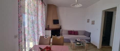 A living room with a sofa, a fireplace, a dining table with chairs, and a television on the wall.